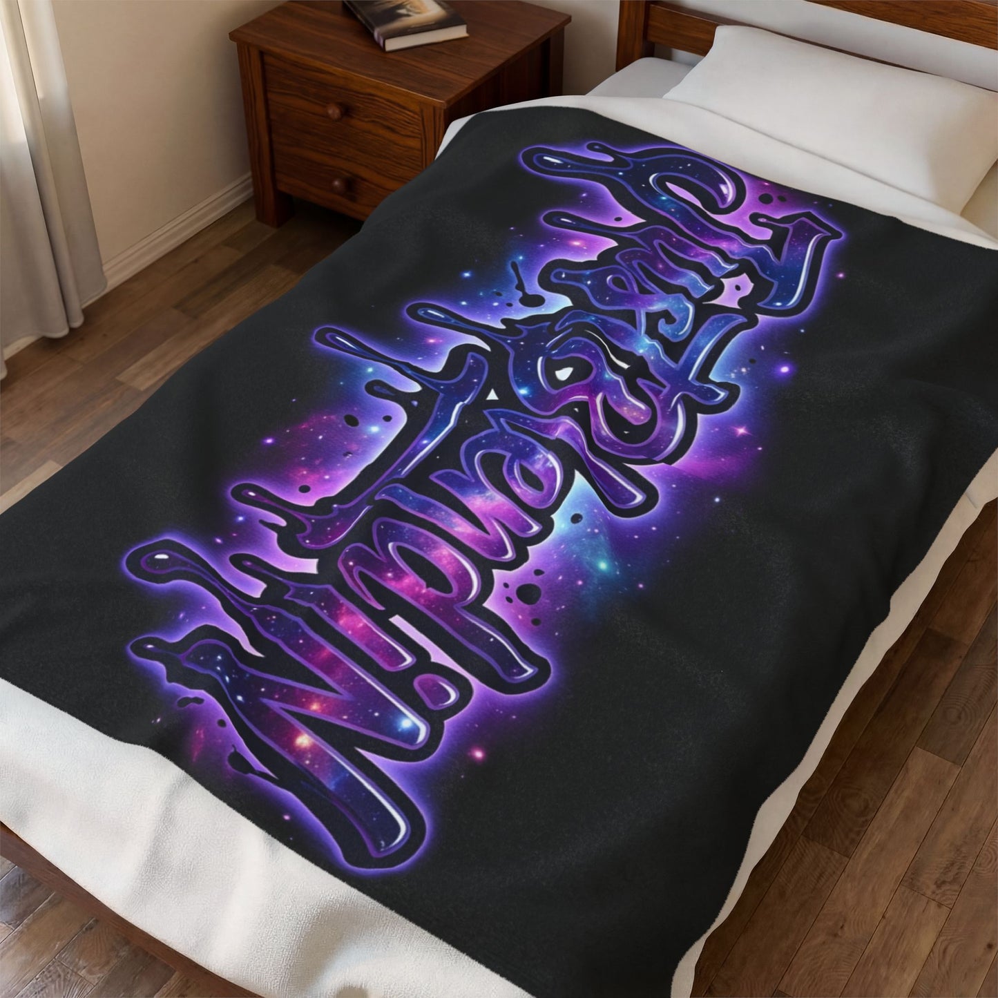 A black fleece blanket with a vibrant purple and blue cosmic graffiti-style graphic reading 'JustBlendiN', styled on a bed in a bedroom setting.